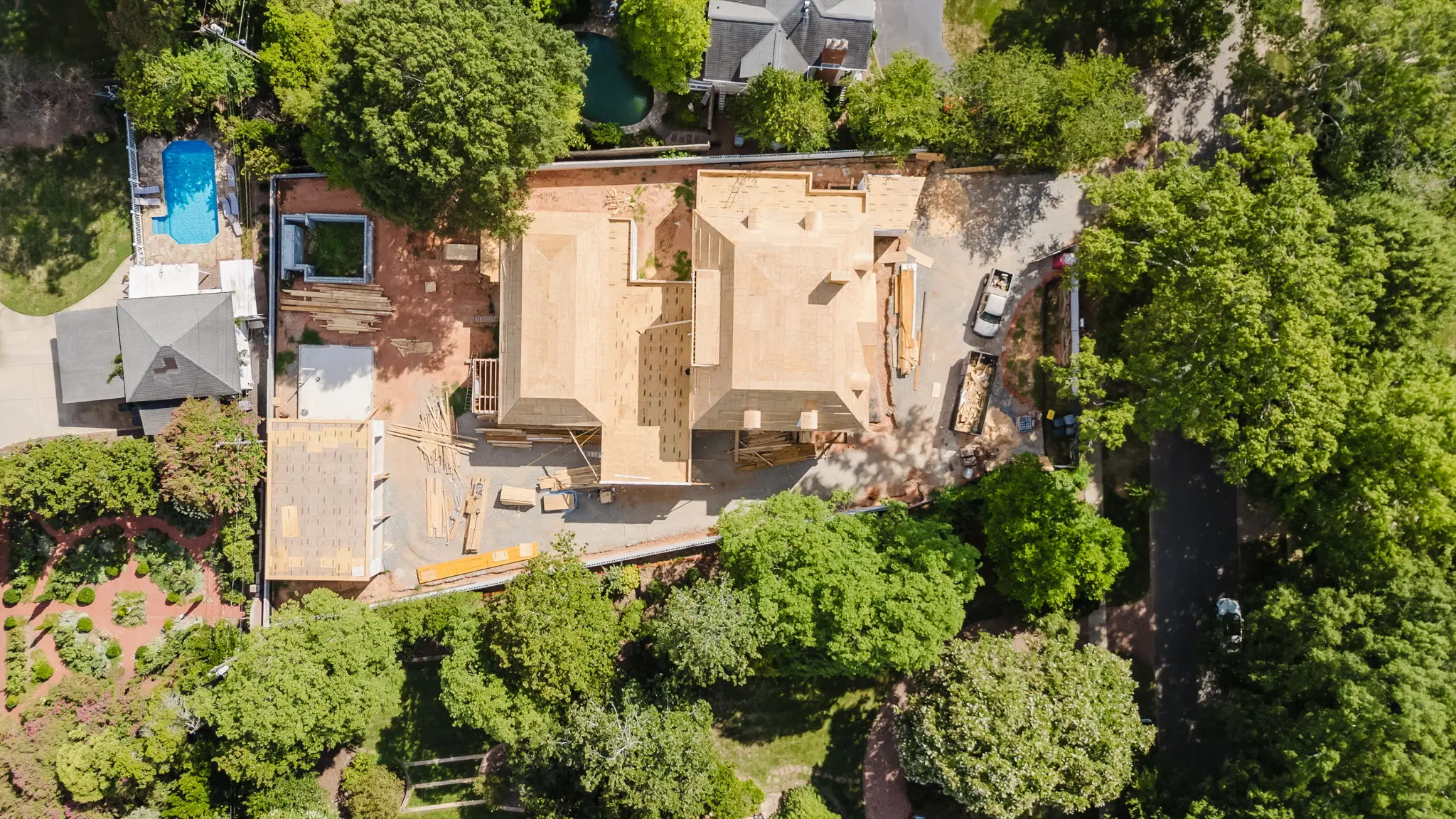 Top-down aerial of a new construction build in progress in Charlotte's 28207 corridor, showing the foundation and roofline relative to the mature canopy lot