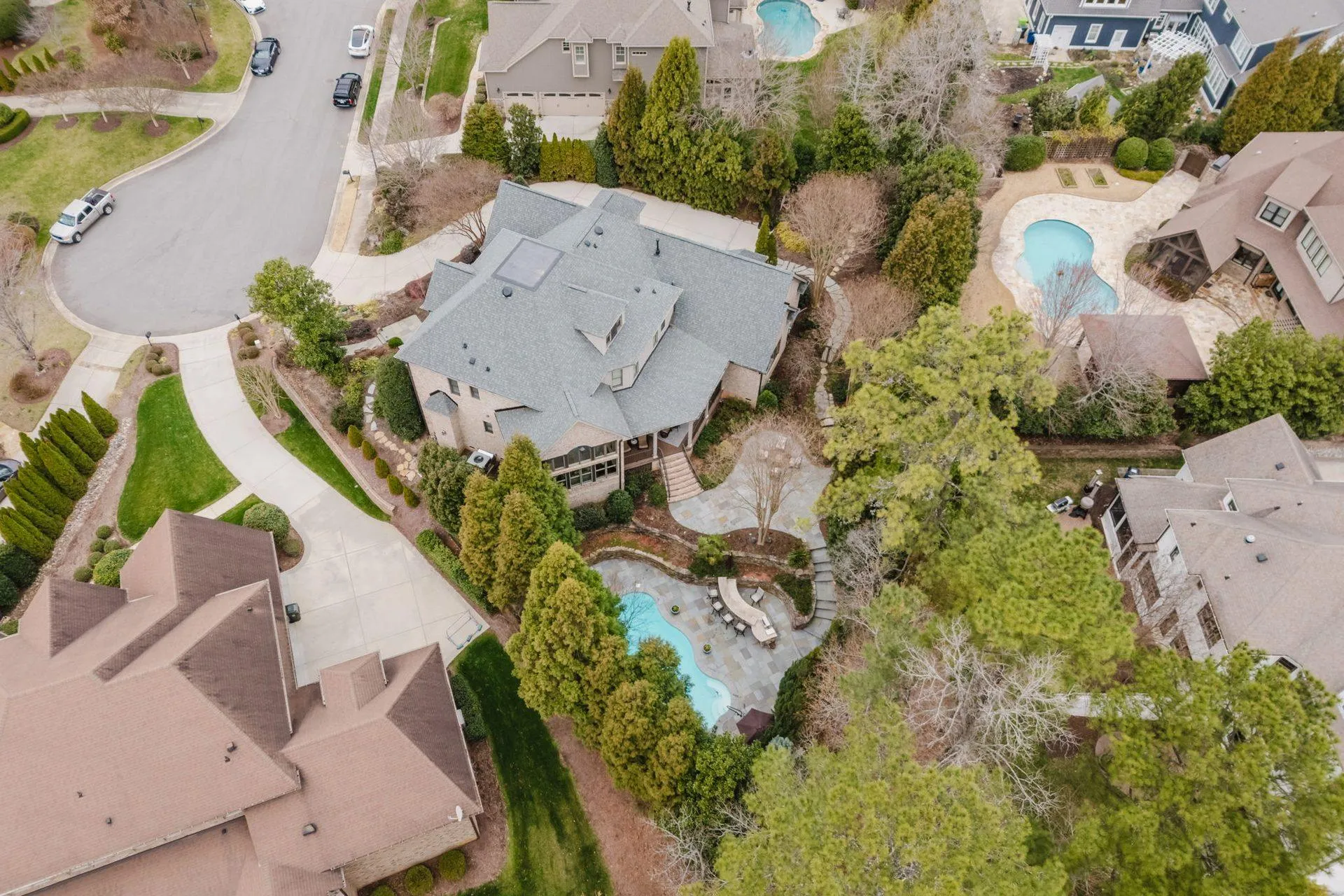 Elevated aerial of 3604 Nightfall Ct showing the pool, roofline, and wooded lot context in a single frame